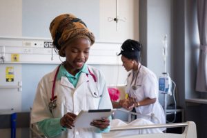 A young African healthcare worker uses a tablet to update and check the patients medical records